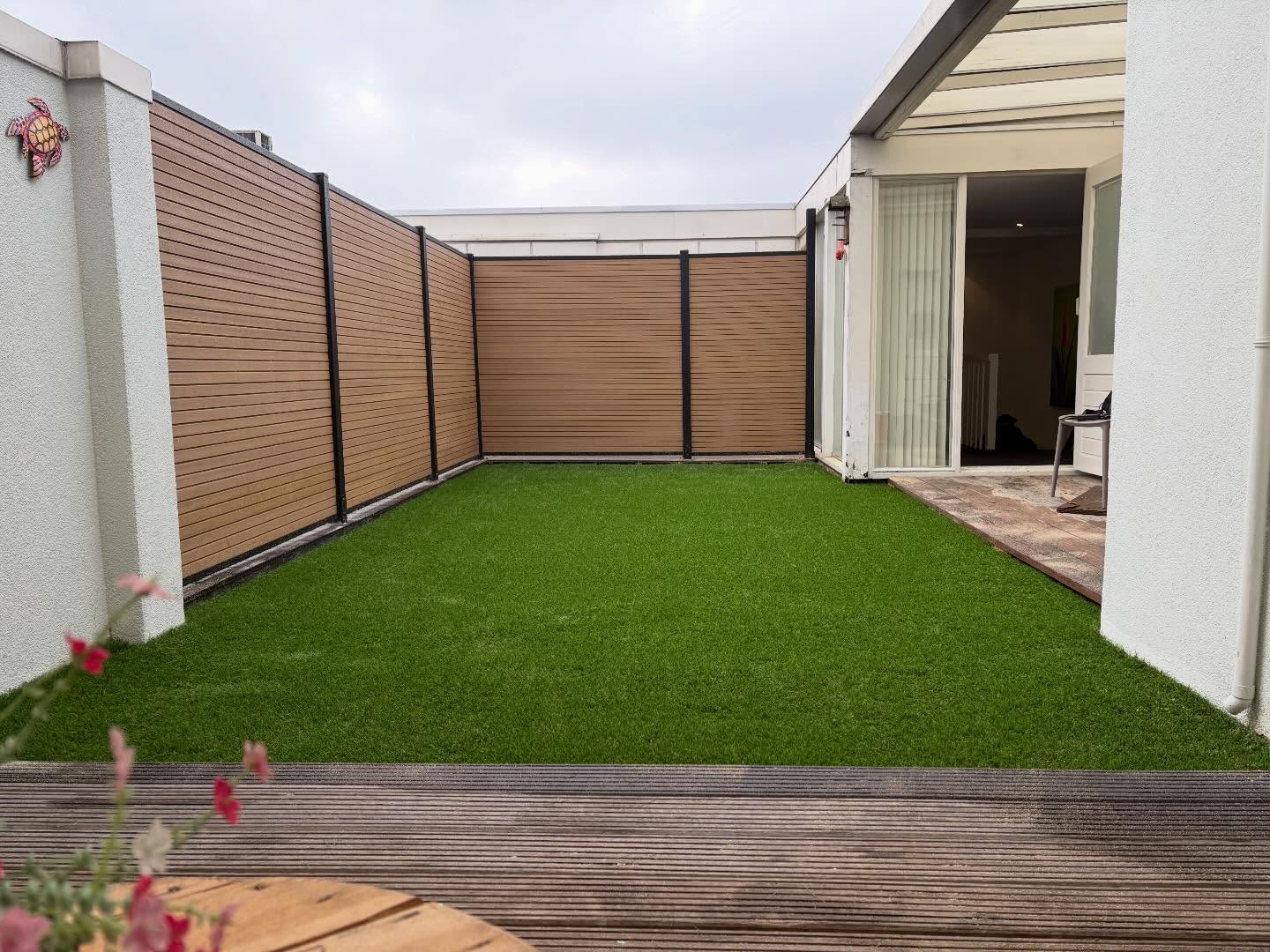 Moderne tuin met kunstgras en houten schutting.