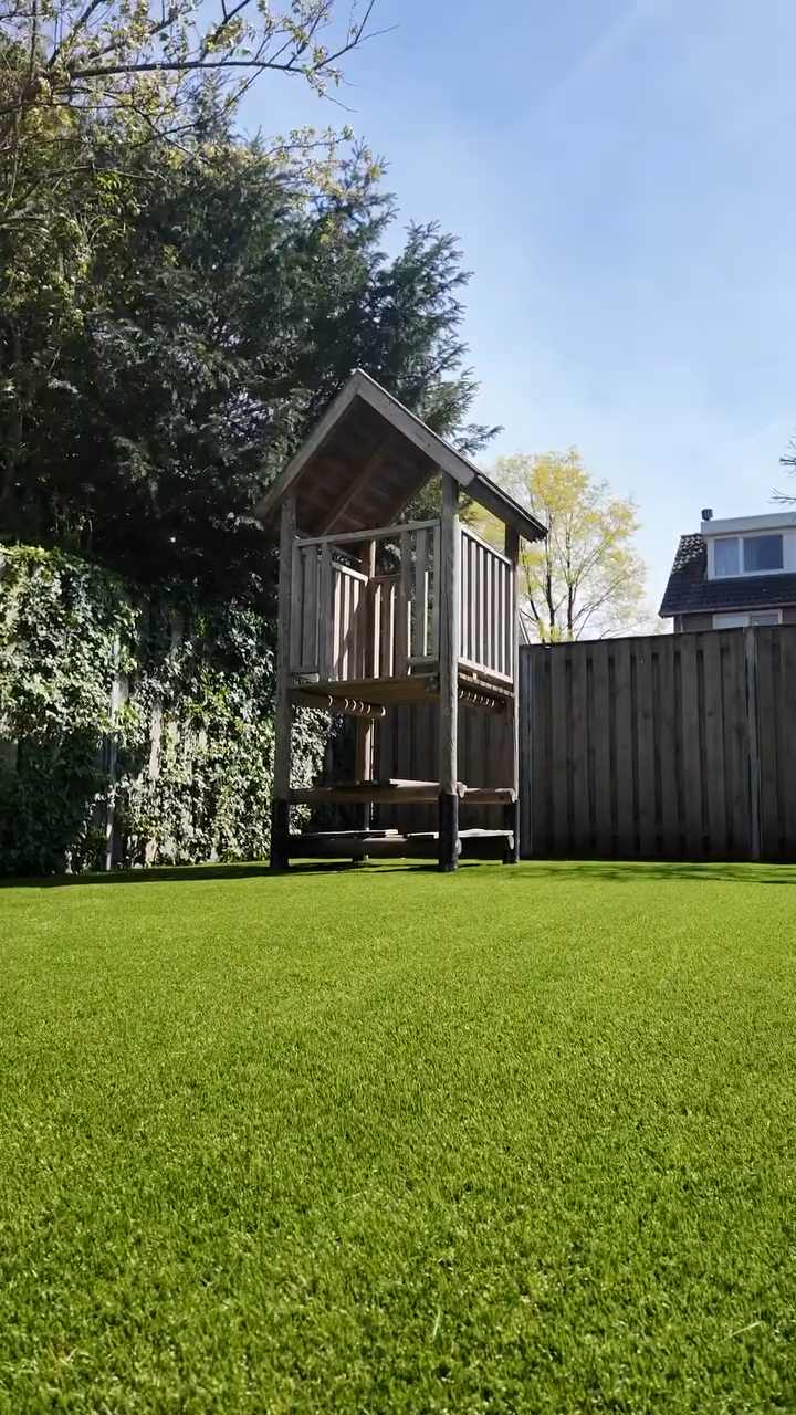 Speelhuisje in zonnige tuin met groen grasveld.